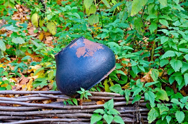 A close-up of a well-maintained compost tumbler in a backyard setting, with visible aeration holes and a convenient handle for turning. The background includes a garden with raised beds and various plants, showcasing an integrated composting and gardening system.