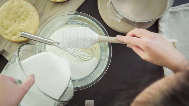 Close-up shot of hands mixing baking soda and vinegar in a glass bowl. The focus is on the bubbling reaction and the natural texture of the ingredients, highlighting the simplicity and purity of DIY cleaning.