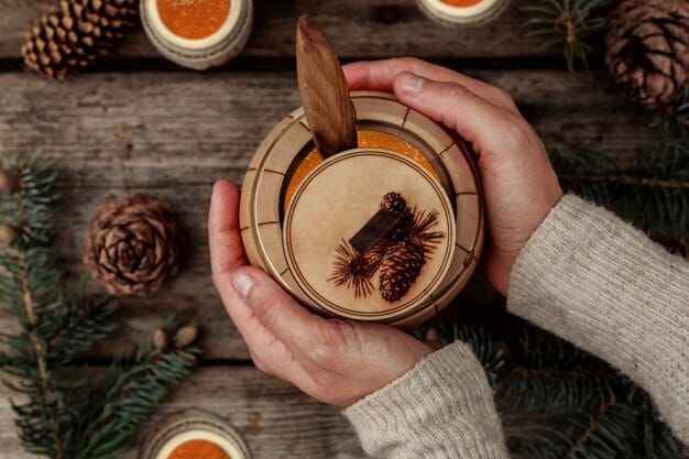 A close-up shot of a person crafting holiday ornaments from natural materials such as pine cones, dried orange slices, and cinnamon sticks on a wooden table.