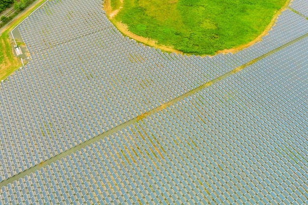 A drone shot of a large-scale solar farm in a rural area, with panels angled towards the sun. The background shows rolling hills and a clear sky, with a transmission line connecting the solar farm to the electrical grid.